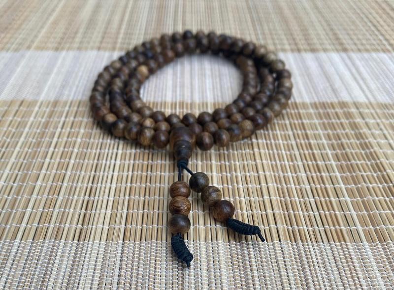 Bàn tay đeo vòng trầm hương kết hợp mặt Phật đang chắp tay cầu nguyện